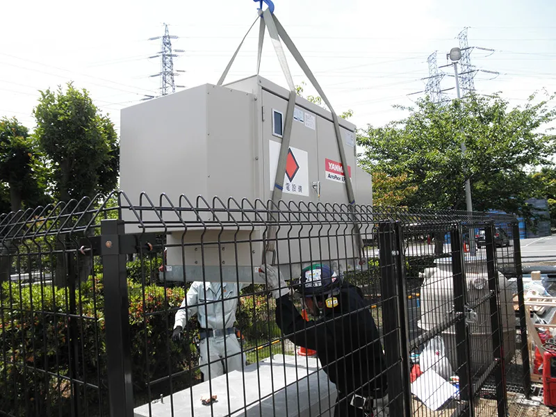 クレーンで電気設備を吊り上げて設置している様子
